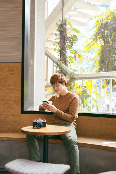 Joven hombre asiático usando el teléfono inteligente durante el desayuno, el café y los conceptos de vacaciones de verano
 - Foto, imagen