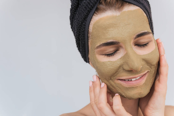 Closeup cropped portrait of young woman applying clay mask on clean face doing beauty wellness treatment on her face skin. Horizontal shot of female applying organic facial mask, with closed eyes. - Фото, изображение