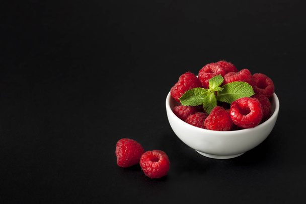 Fresh raspberries in a bowl with mint on black background - Fotó, kép