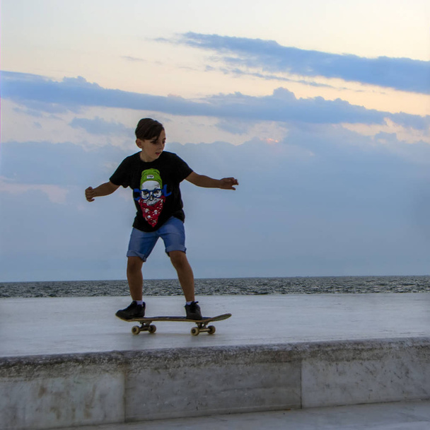 thessaloniki, griechenland - 06. Juli 2018: Ein junger Skateboarder macht einen Skateboard-Trick auf der Marmoroberfläche mit Meereshintergrund bei Sonnenuntergang - Foto, Bild