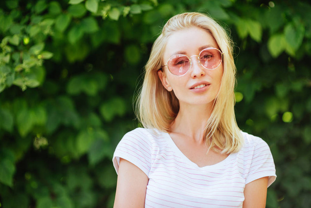 Outdoors lifestyle fashion portrait of beautiful woman smiling and enjoying nature in the park. Wearing stylish sunglasses, t-shirt. Summertime - Fotó, kép
