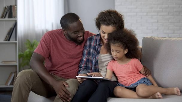 Parents showing daughter her first photos on tablet, cozy family atmosphere - Fotoğraf, Görsel