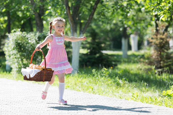 A little girl runs along the street in the city with bread and baking. The girl runs along the road with a basket of bread. - Fotoğraf, Görsel