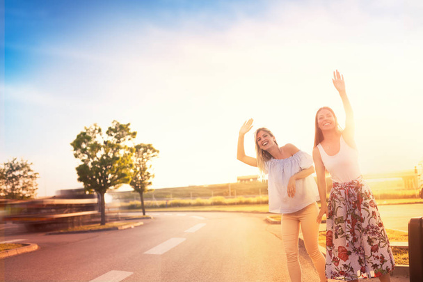 Two friends on a road trip, hipster girls hitchhiking on roadside of highway - Foto, Imagem