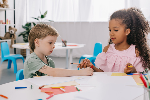 retrato de pré-escolares multiculturais à mesa com papéis e lápis em sala de aula
 - Foto, Imagem