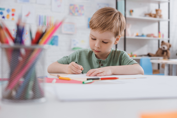 portrait of preschooler drawing picture with pencils at table in classroom - Photo, Image