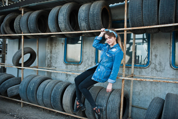Joven chica hipster en chaqueta jeans y bufanda en la zona de montaje de neumáticos
. - Foto, Imagen