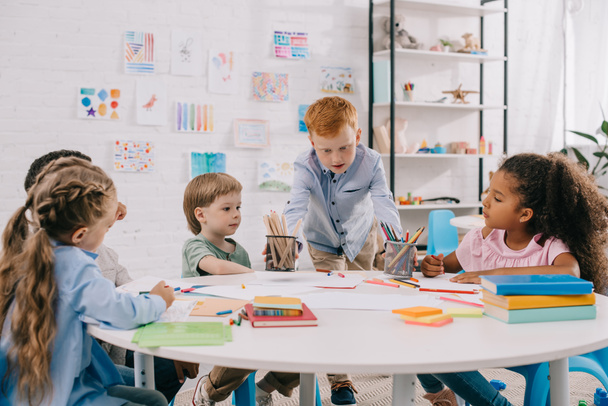 Kinder sitzen mit Papieren und Farben am Tisch, um im Klassenzimmer zu zeichnen - Foto, Bild