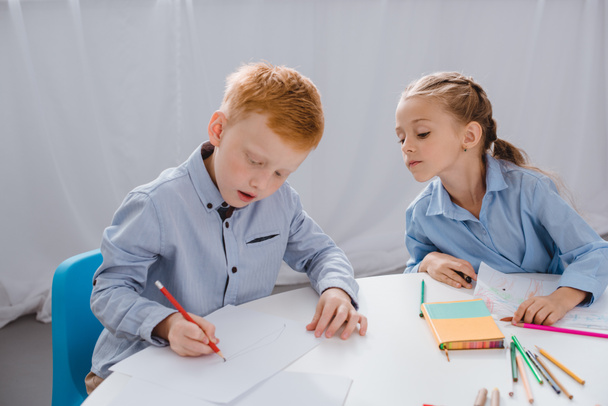 Porträt entzückender Kinder, die Bilder am Tisch im Klassenzimmer zeichnen - Foto, Bild