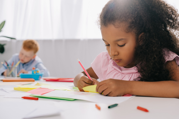 selective focus of multicultural preschoolers drawing pictures with pencils in classroom - Fotoğraf, Görsel
