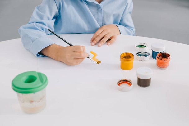 частковий вигляд дитячого малюнка з фарбами та пензлем за столом
 - Фото, зображення