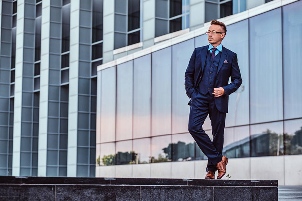 Full body portrait of a confident man in an elegant suit posing with hand in pocket against skyscraper background. - Foto, immagini
