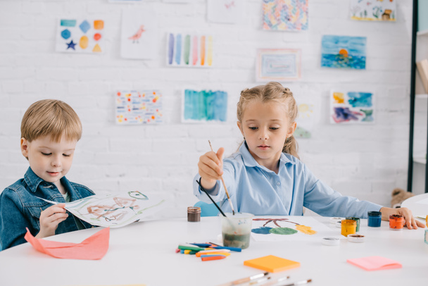 koncentrált óvodás gyerekek rajz-képek, festékek és ecsetek-asztalnál osztályteremben - Fotó, kép