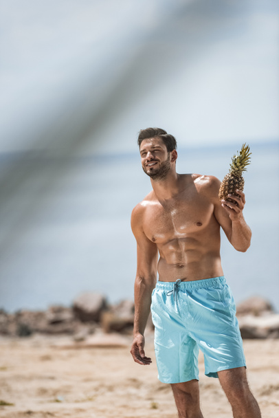 happy shirtless man holding pineapple on sea beach  - Fotó, kép