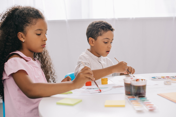 fokussierte afrikanisch-amerikanische Kinder malen Bilder mit Farben und Pinseln im Klassenzimmer - Foto, Bild