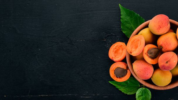 Fresh apricots with leaves On a black wooden background. Top view. Free space for your text. - Foto, Imagen