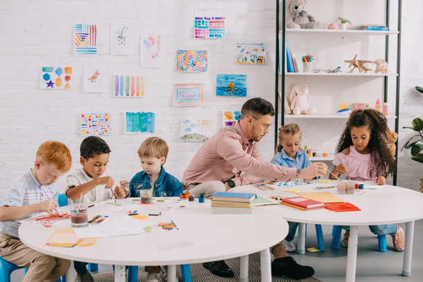maestro y niños interracial dibujando juntos en las mesas en el aula
 - Foto, imagen