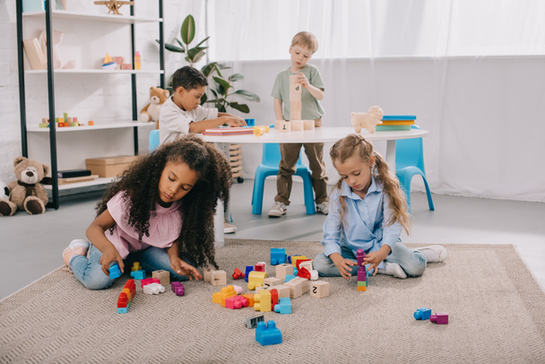 focused multiracial preschoolers playing with wooden blocks in classroom - Zdjęcie, obraz