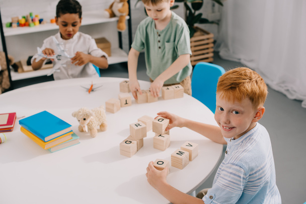 multicultural little boys plying with wooden blocks at table in classroom - Foto, Imagem