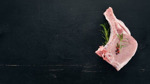 Raw steak on the bone with spices and vegetables. On a wooden background. Top view. Copy space. - Фото, изображение