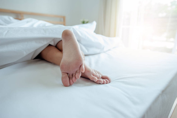 Young female sleeping in bed at home with focus on legs. Feet of woman lying on bed. - Foto, afbeelding