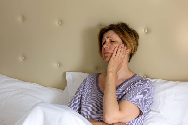Une femme se sent malade, s'assoit au lit le matin. Mal de tête. Maux de dents
. - Photo, image