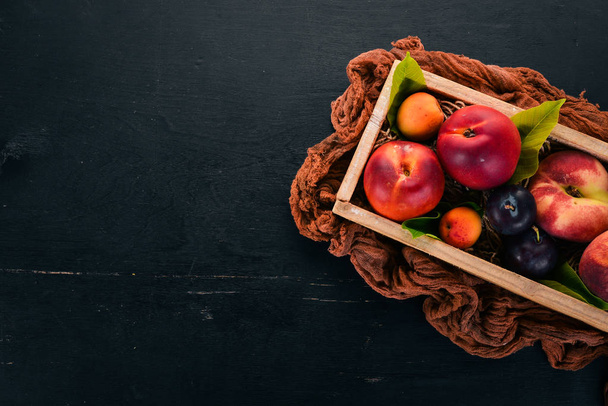 Fresh fruits in a wooden box. Apricot, peach, nectarine, plum. On a wooden background. Top view. Free space for your text. - Photo, Image