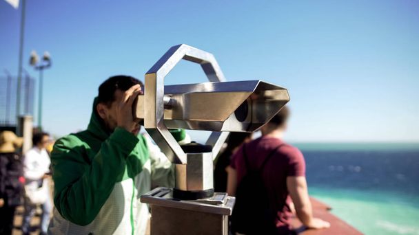 Turista mirando a través de prismáticos en la plataforma de observación, hombre admirando el paisaje marino
 - Foto, imagen