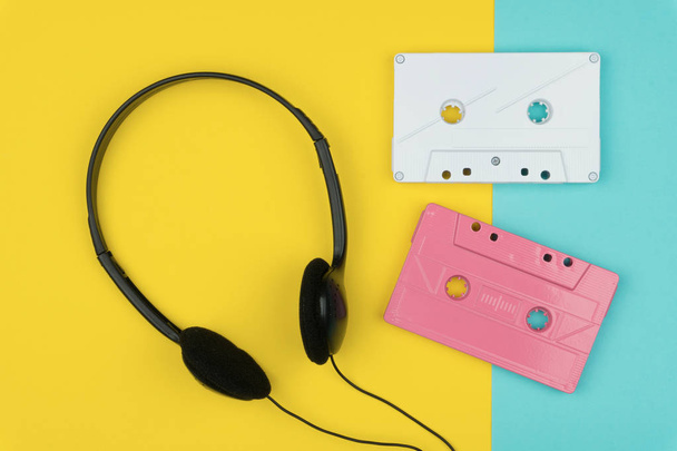 top view of the white and pink audio cassette tapes with the black headphone on yellow and blue background - Photo, Image