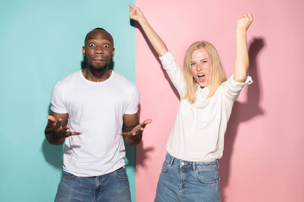 We won. Winning success happy afro man and woman celebrating being a winner. Dynamic image of caucasian female and male model on pink studio. - Foto, Imagem