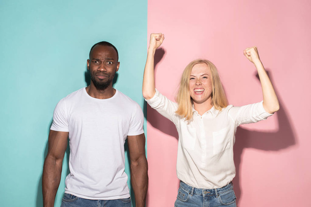 We won. Winning success happy afro man and woman celebrating being a winner. Dynamic image of caucasian female and male model on pink studio. - Foto, Imagen