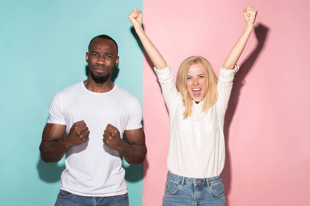We won. Winning success happy afro man and woman celebrating being a winner. Dynamic image of caucasian female and male model on pink studio. - Foto, imagen