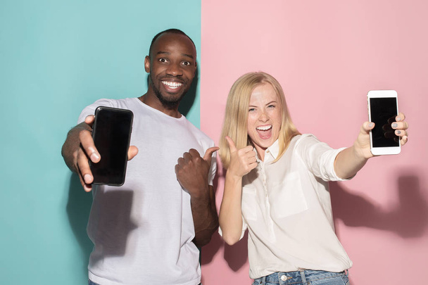 Portrait of a confident casual girl showing blank screen mobile phone and afro man - Φωτογραφία, εικόνα