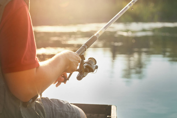 Fishing rod wheel close up, man fishing with a beautiful sunrise behind him - Foto, Bild