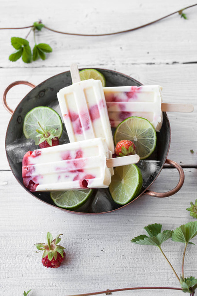 Delicious popsicles made with strawberries and lime in bowl on wooden table - Foto, afbeelding