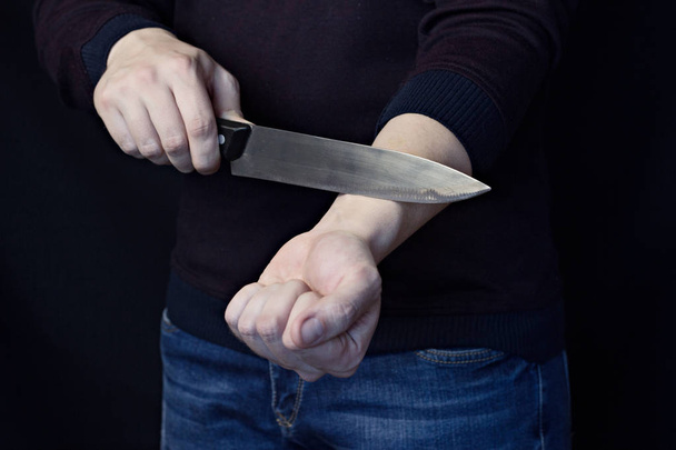 A man is cutting a vein on his hand, a black background - Foto, Bild