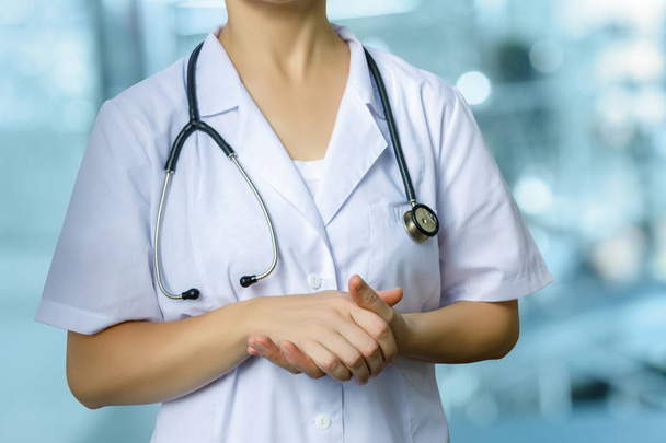 Verpleegkundige permanent met gevouwen handen op de onscherpe achtergrond. - Foto, afbeelding