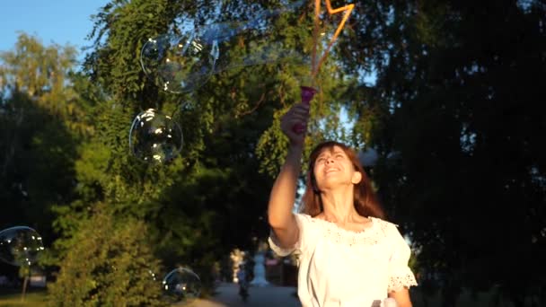 menina alegre ri e lança grandes bolhas de sabão no parque da cidade e sorri. Movimento lento
. - Filmagem, Vídeo