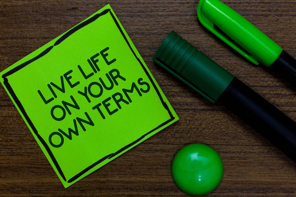 Text sign showing Live Life On Your Own Terms. Conceptual photo Give yourself guidelines for a good living Written on sticky note two markers laid on wooden floor green ball - Photo, Image