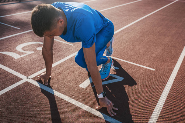 Side view of young male athlete at starting block on running track. Caucasian sprinter man in starting position for running to start a race at stadium. Sport, lifestyle and people concept. - Fotoğraf, Görsel