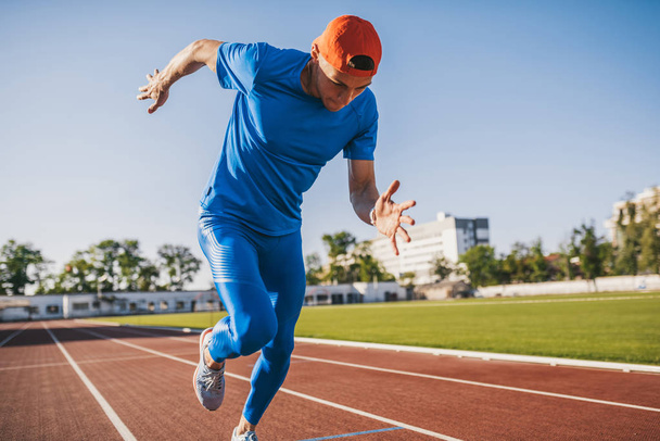 Handsome professional young Caucasian male athletic running and jogging alone along a race track in stadium while out training on a sunny day. Sport, lifestyle and people concept. - Fotoğraf, Görsel