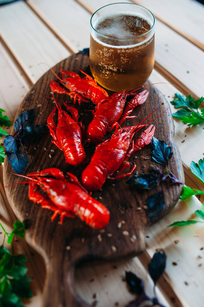 Красные раки варят на кухонной доске с базиликовым укропом и бокалом пива
 - Фото, изображение