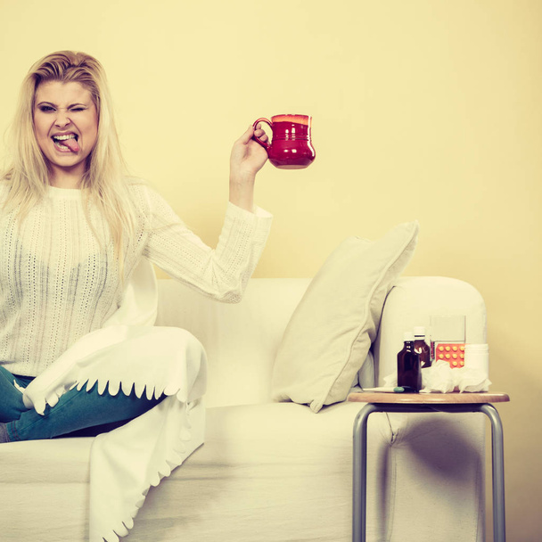 Päästä eroon kuumeesta ja kausittaisesta sairaudesta. Onnellinen nainen osoittaa kupin teetä istuu sohvalla pöydän vieressä lääkkeiden ja pillereiden kanssa
. - Valokuva, kuva