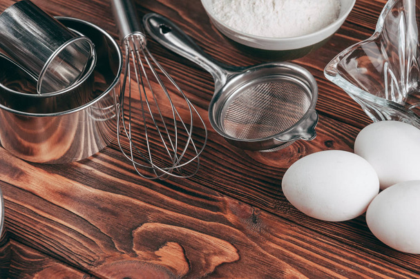 Ingredients in the dishes on a wooden brown table, where as well lie the whisk is full for flour, three chicken eggs and a slate board. View from above. Place under the text - 写真・画像