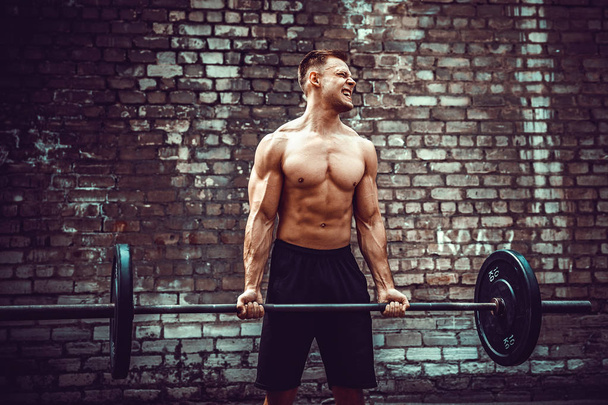 Athletic man working out with a barbell. Strength and motivation. Biceps exercise. - 写真・画像