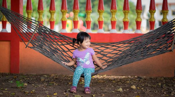 маленька азіатська дівчинка у фіолетовій сорочці сидить на колисці
 - Фото, зображення