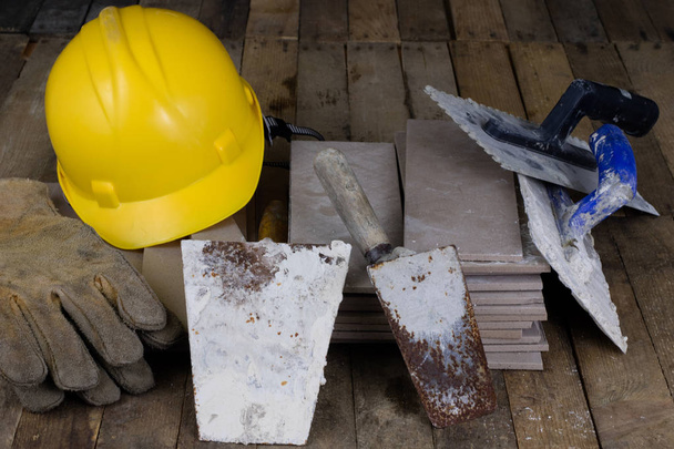 Casco, baldosas y herramientas para el constructor. Accesorios para los trabajadores de la construcción en una mesa de taller de madera. Fondo oscuro
. - Foto, imagen