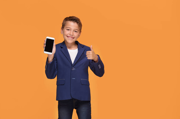 Little boy with smartphone at orange studio background, copy space. Happy child in formal suit playing adult businessman. - Foto, immagini