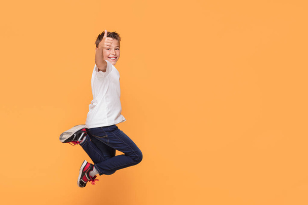 Little school boy jumping in the studio on a yellow background. Concept of happy childhood. - Photo, image