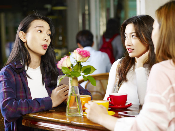 drei glückliche schöne junge asiatische Frauen sitzen am Tisch und unterhalten sich im Café oder Teehaus. - Foto, Bild